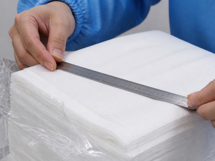 airlaid napkin manufacturer — close-up of a white airlaid napkin fold edge being checked with a simple metal ruler after pack