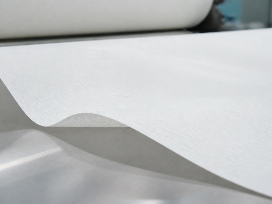 airlaid paper supplier — close-up side view of an airlaid paper web edge lifting slightly above a flat stainless reference