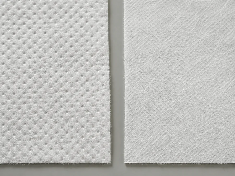Two white nonwoven wipe samples showing embossed and cross-laid surface textures