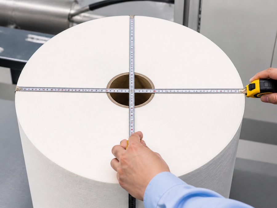 TAD tissue jumbo rolls — close-up diameter measurement across a large white tissue roll using a tape at two perpendicular