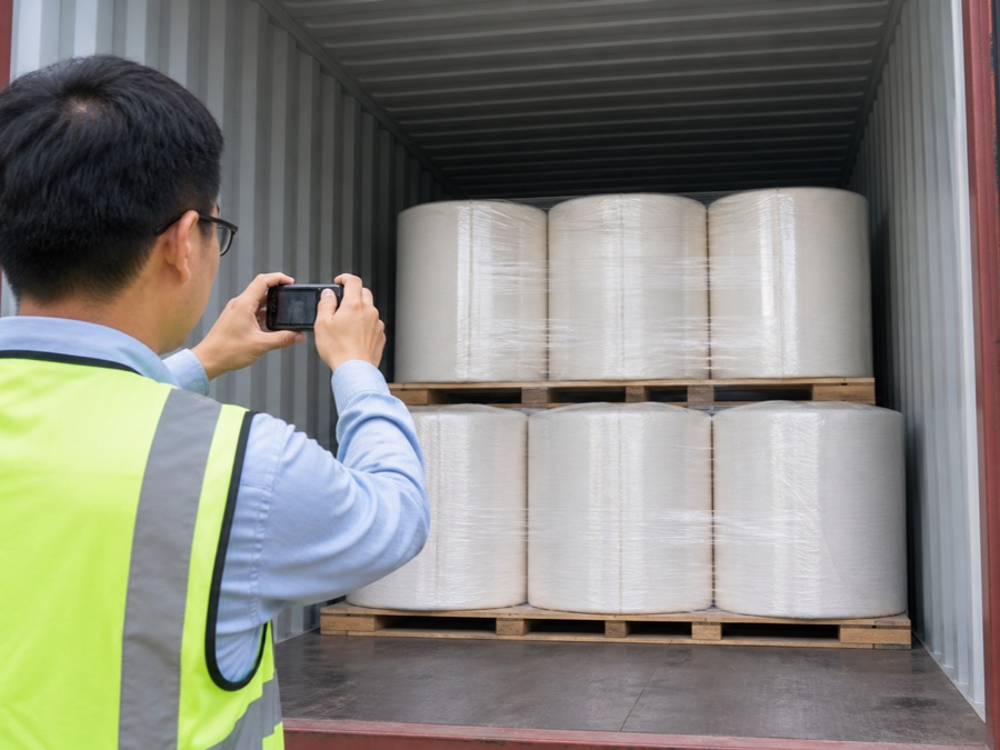 tissue mother roll supplier — Chinese adult logistics inspector in safety vest photographing a container interior before the doors