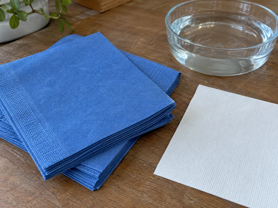Blue folded airlaid napkins beside white paper and a water dish