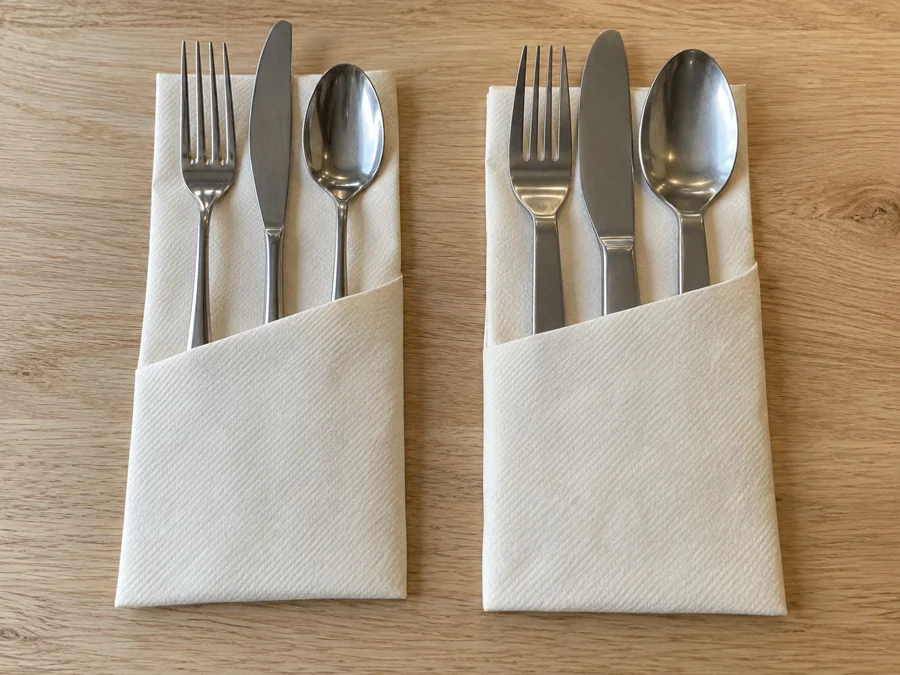 Two ivory napkin pockets holding different stainless steel cutlery sets